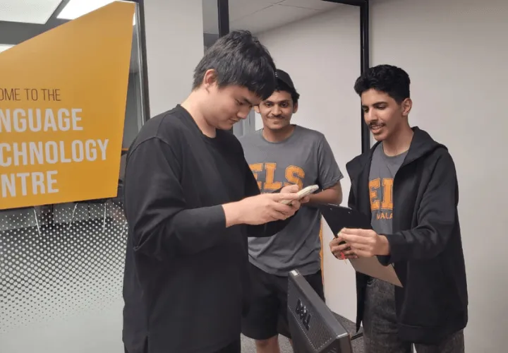 A trio of ELS students huddling together in the midst of a class activity